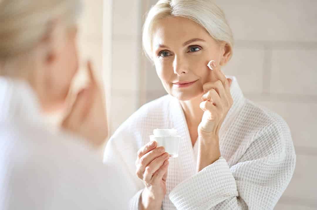 mature woman applying skin cream to her face