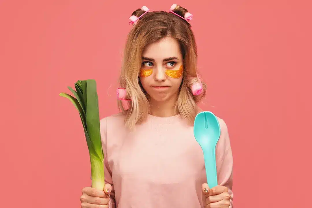 Young woman with rollers in her hair holding a plastic spoon and green vegetable.