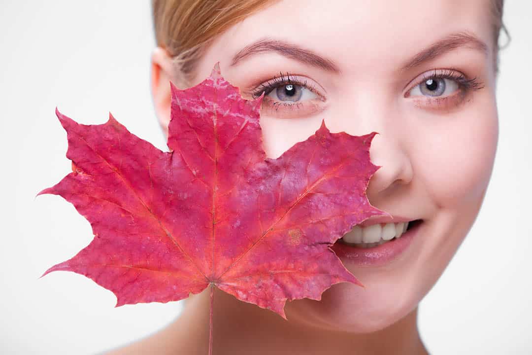 Young woman holding a red maple leaf in front of her face