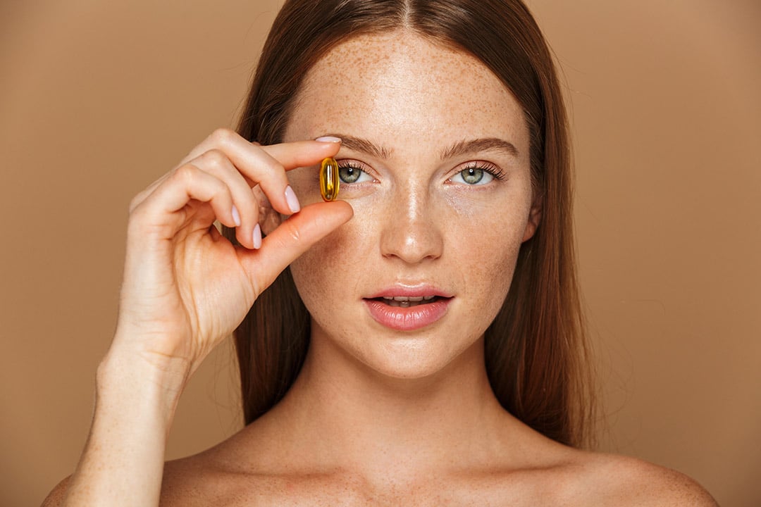 Young woman holding a yellow multivitamin capsule in front of her face