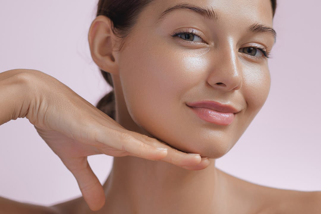 Young woman smiling and touching her jawline while she smiles at the camera