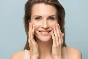 Middle aged woman smiling at the camera while touching her face