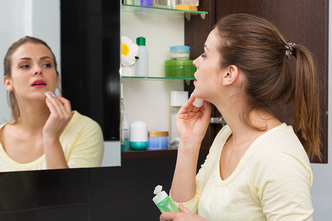 A woman looking at herself in the mirror while touching her chin
